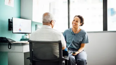 Female HCP taking male patient blood pressure with a smile on her face