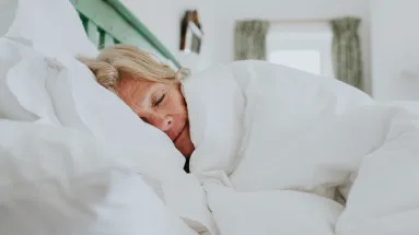 Woman sleeping in bed under white comforter
