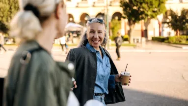 Woman walking with another woman while holding coffee and smiling