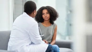 Young woman sitting next to lady in physicians jacket, back is turned t