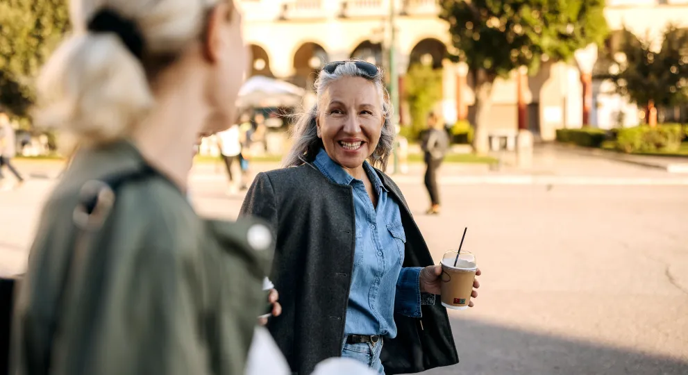 Woman walking with another woman while holding coffee and smiling