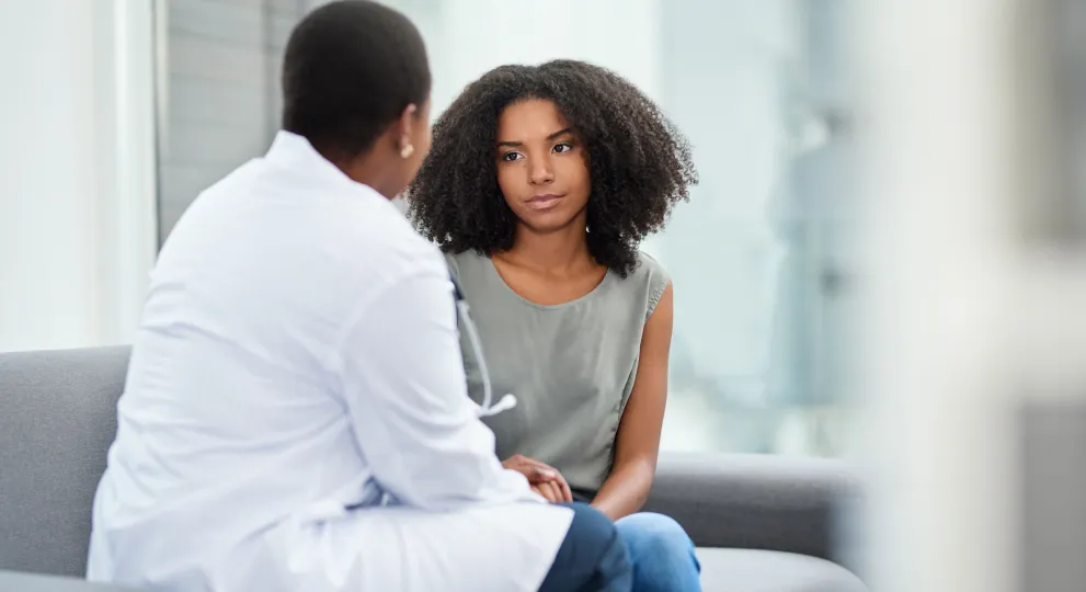 Young woman sitting next to lady in physicians jacket, back is turned t