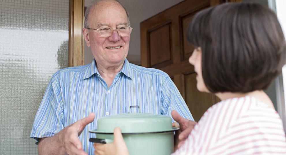A man receiving a pot of food from a neighbor at the door